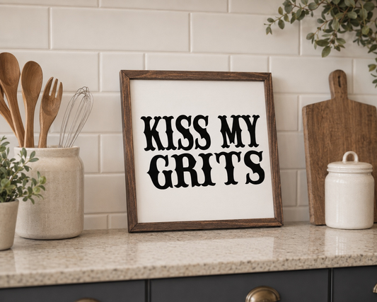 Kitchen counter with a framed sign reading 'Kiss My Grits' against a tiled wall.