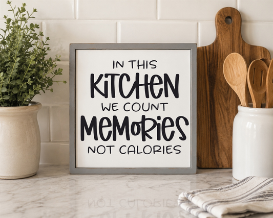 Framed sign in a kitchen with text 'In this kitchen we count memories not calories', surrounded by kitchen items.
