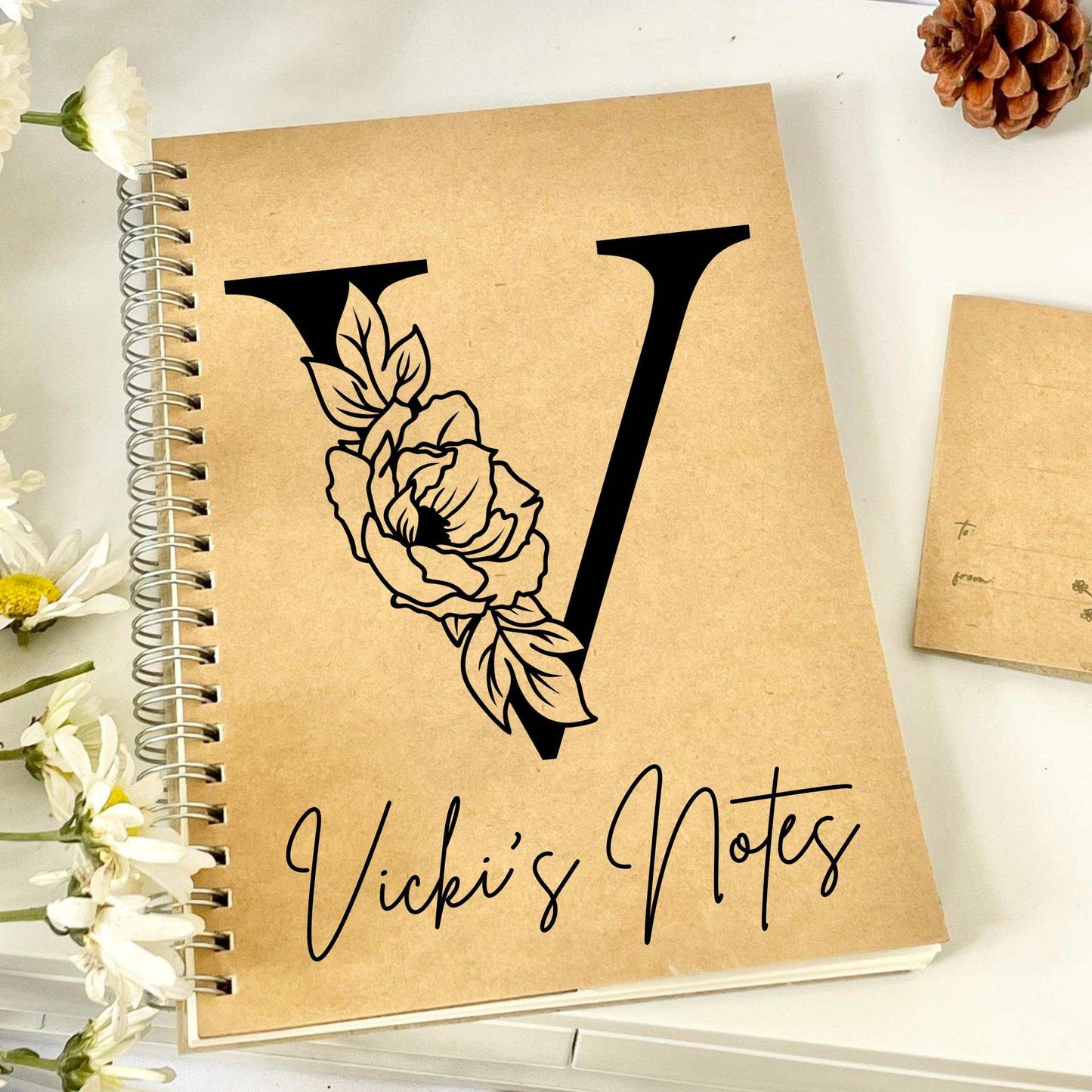 Personalized monogrammed notebook with floral design on kraft cover.