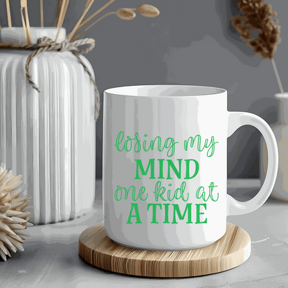Ceramic mug with "Losing My Mind One Kid at a Time" text, 15 ounces, humorous gift for moms, white and glossy.