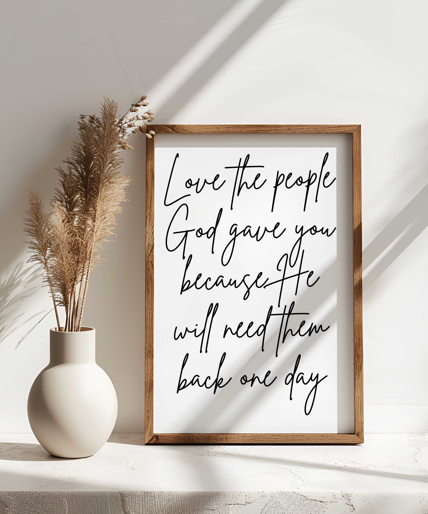 Handcrafted farmhouse wood sign with "Love the people God gave you because He will need them back one day" script wall art in a sturdy frame next to decorative vase with pampas grass.
