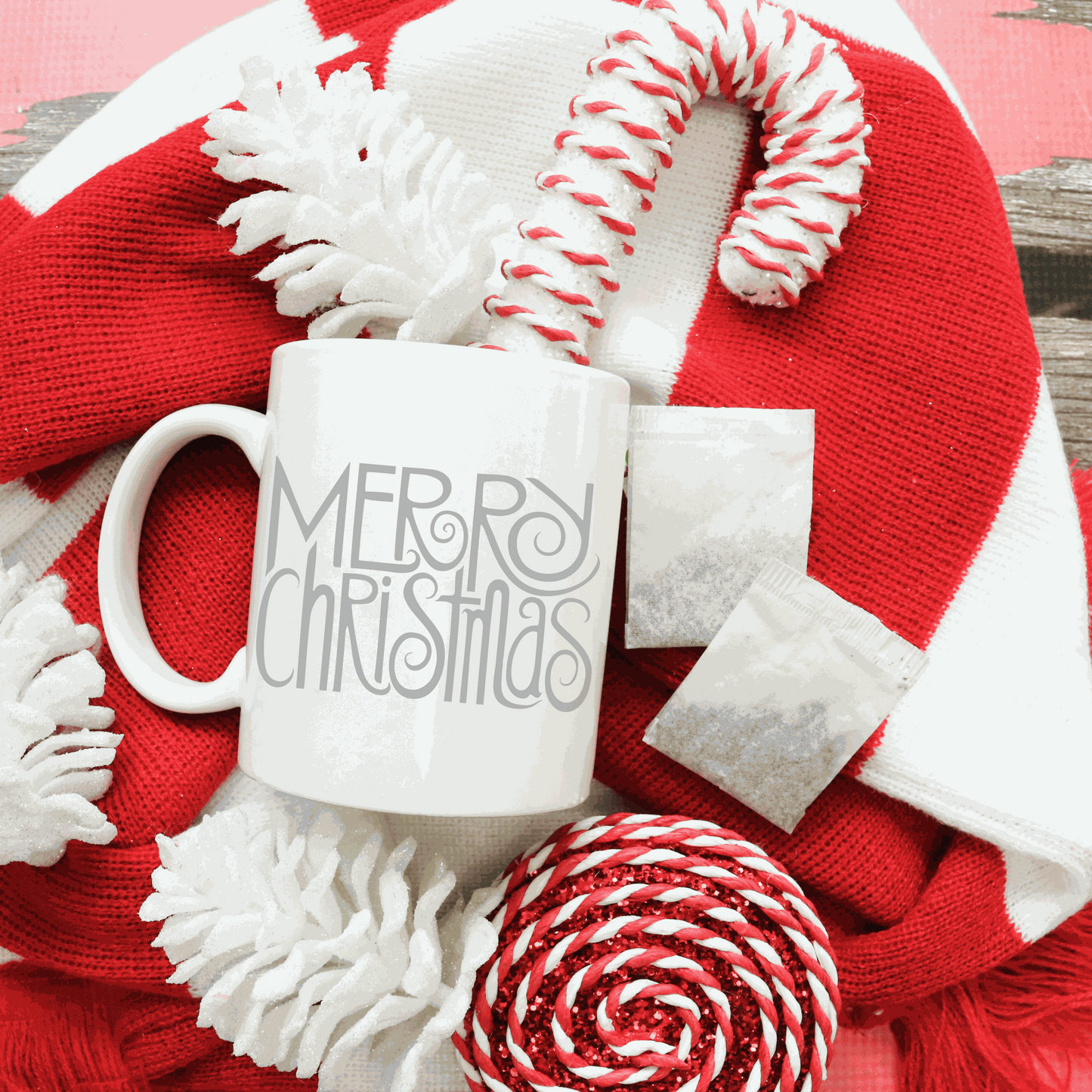 Merry Christmas white ceramic mug with festive candy canes and red scarf background.