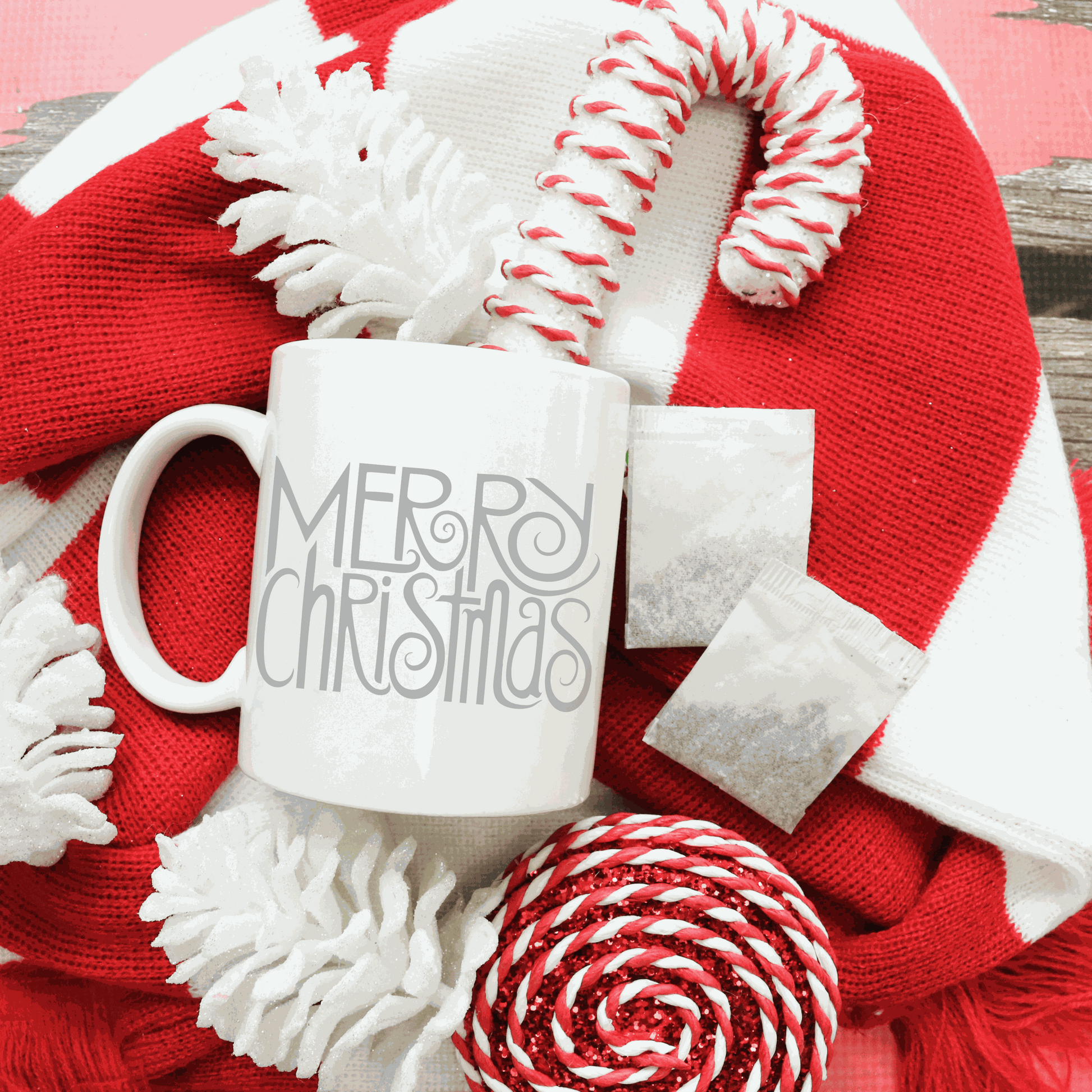 Merry Christmas white ceramic mug with festive candy canes and red scarf background.