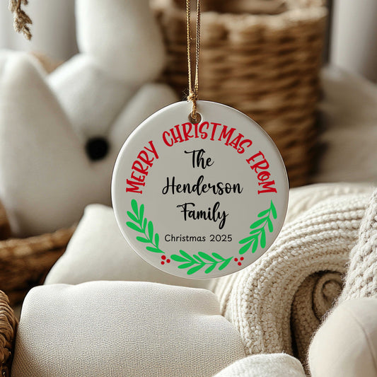 Personalized round ceramic Christmas ornament with family name and year, decorated with festive red and green design, hanging with gold string