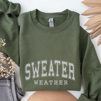 Folded olive green crewneck sweatshirt with "Sweater Weather" embroidery, styled for cozy fall fashion.