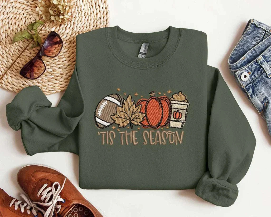 Autumn-themed sweatshirt with embroidered pumpkin spice latte, football, maple leaf, and pumpkin graphic, 'Tis the Season' text.