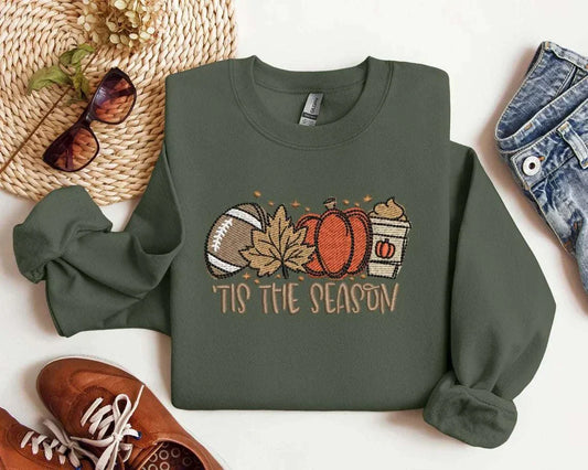 Autumn-themed sweatshirt with embroidered pumpkin spice latte, football, maple leaf, and pumpkin graphic, 'Tis the Season' text.