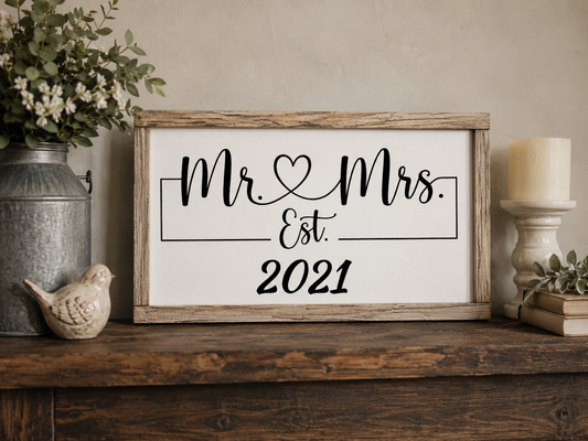 Decorative sign with 'Mr Mrs Est. 2021' on a wooden shelf with plants and a candle.