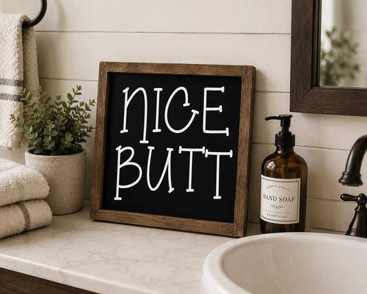 Bathroom counter with a sign reading 'NICE BUTT', hand soap, and plants.