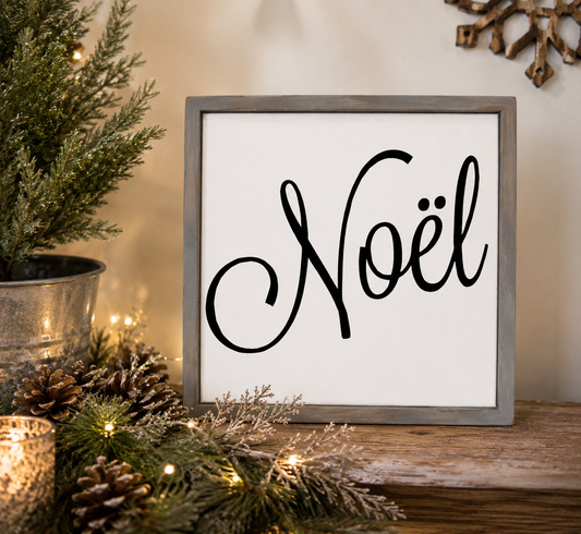 Framed 'Noél' sign with Christmas decorations on a wooden surface.