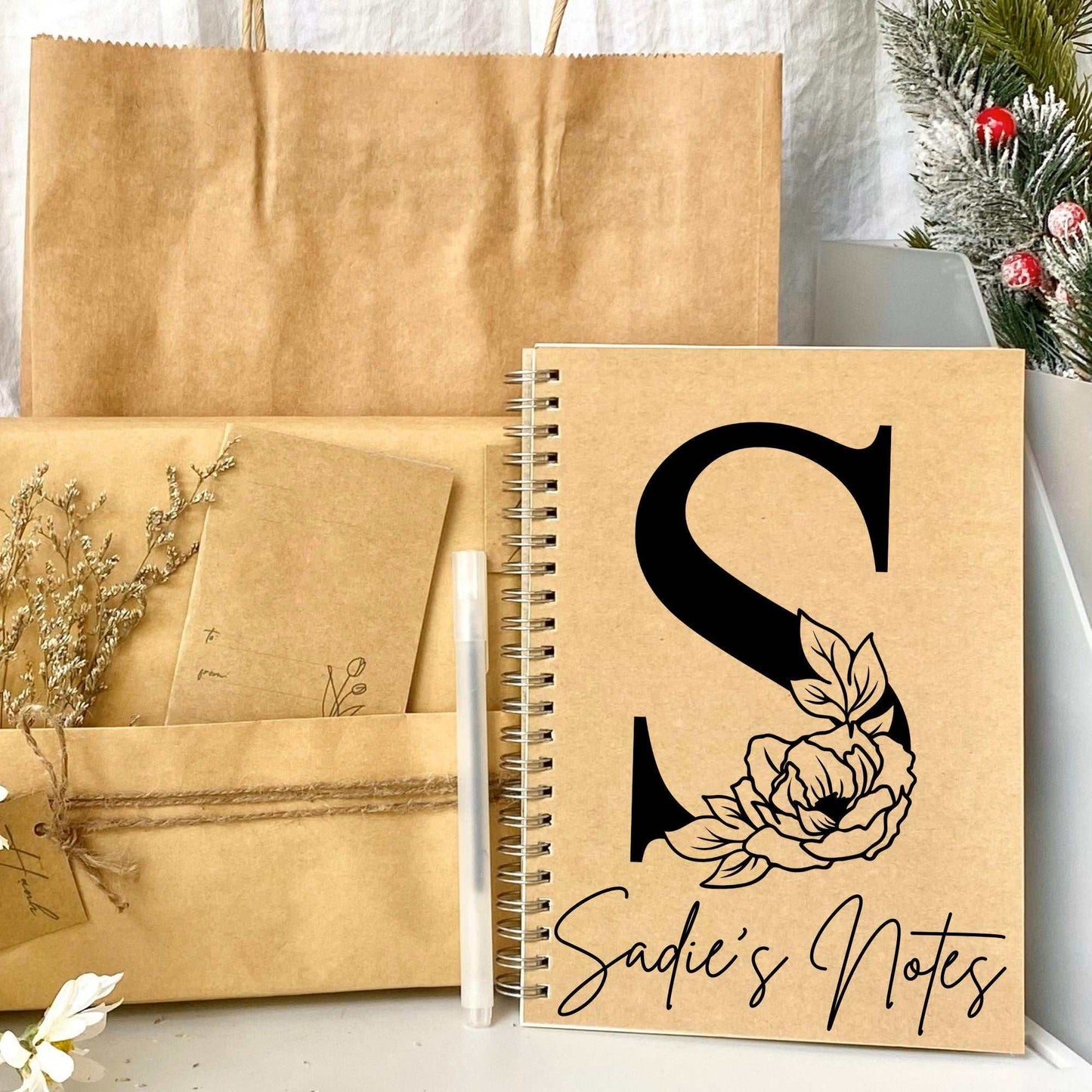 Unique monogrammed notebook with floral design on kraft paper cover, featuring personalized initial and name, spiral bound, portable size.