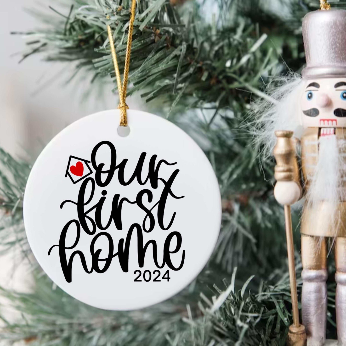 Personalized "Our First Home 2024" round Christmas ornament hanging on tree with nutcracker decoration