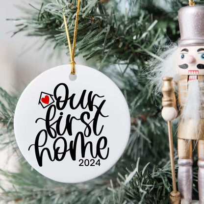 Personalized "Our First Home 2024" round Christmas ornament hanging on tree with nutcracker decoration