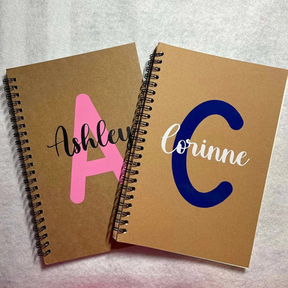 Personalized spiral notebooks with kraft cover, featuring names Ashley and Corinne, 8.3 x 5.5 inches.