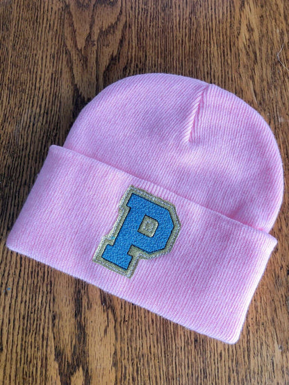 Custom pink embroidered initial beanie with blue 'P' on wooden surface.
