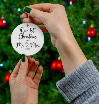 Personalized round porcelain Christmas ornament reading "Our 1st Christmas as Mr. & Mrs." hanging on a tree with gold string