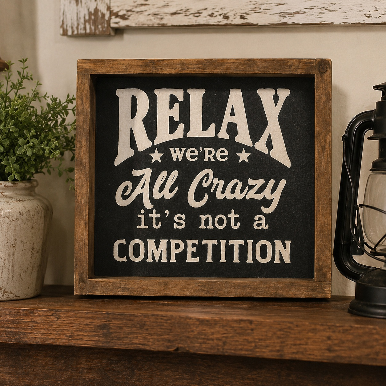 Decorative sign with text 'Relax, we're all crazy, it's not a competition' on a wooden surface.