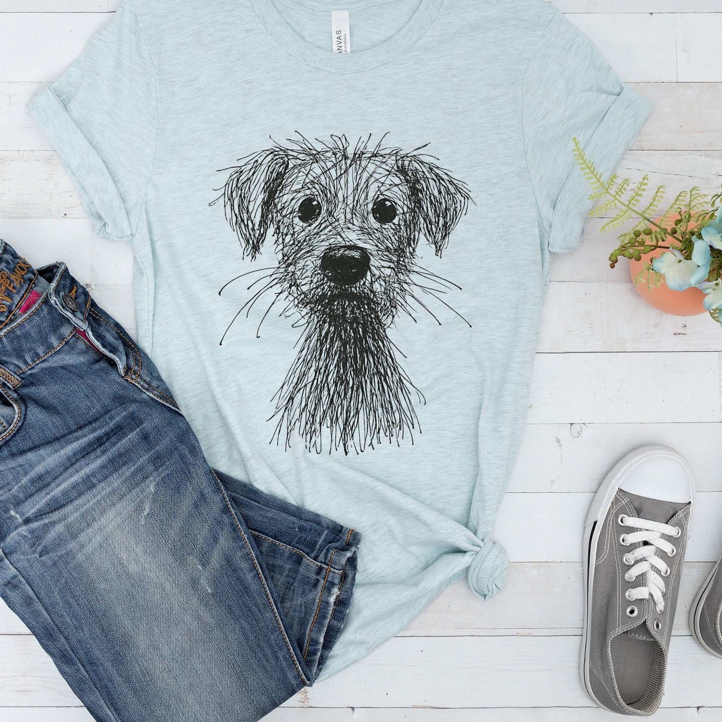 Light blue women's casual t-shirt with black scribble sketch dog graphic, paired with blue jeans and gray sneakers.