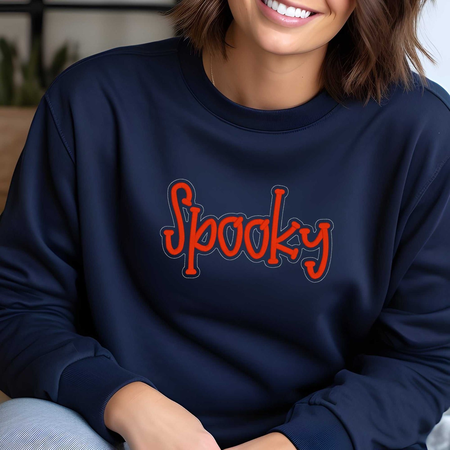 woman wearing navy blue cozy crewneck sweatshirt with embroidered orange "Spooky" text for fall Halloween style