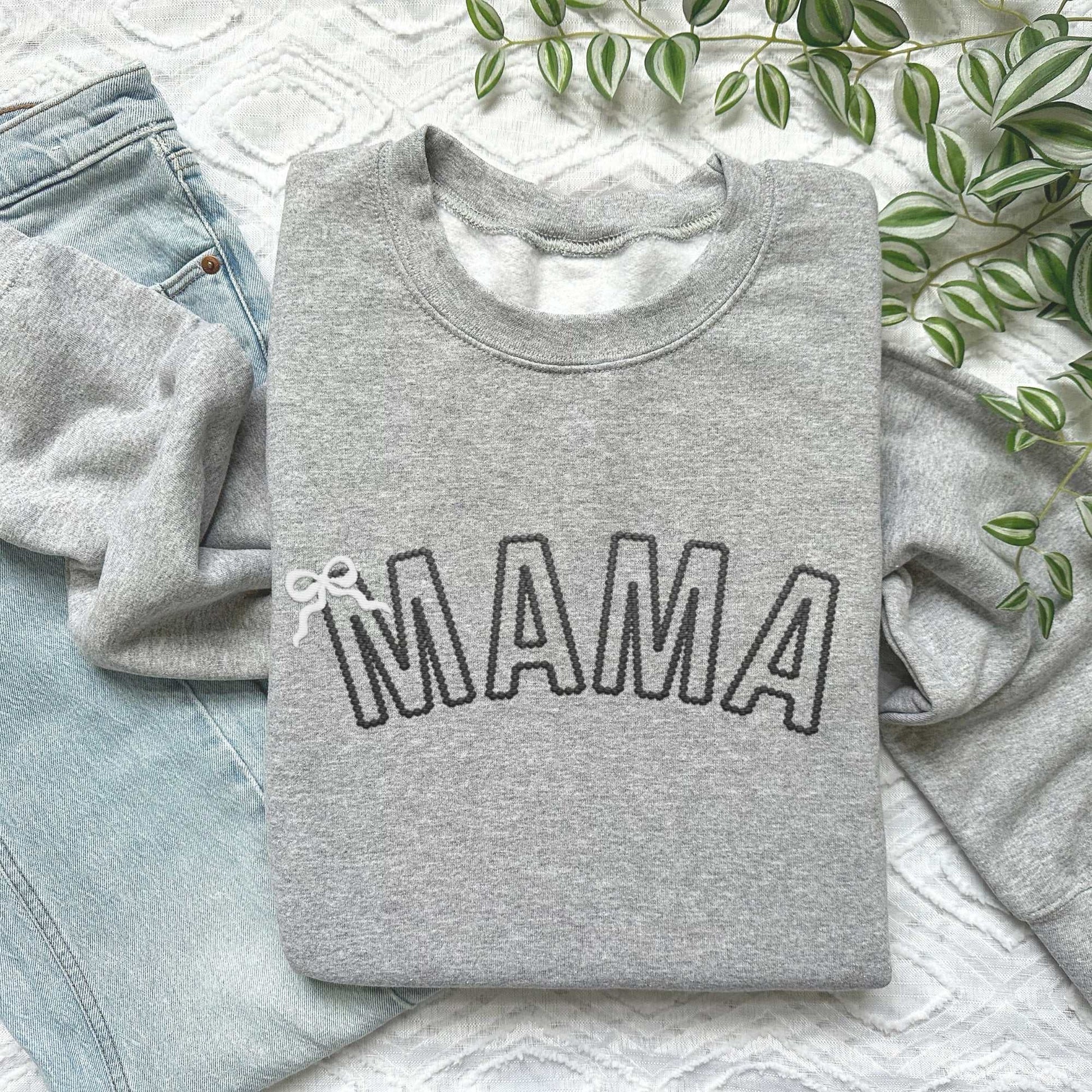 Custom embroidered "MAMA" sweatshirt in gray with bow detail on a textured background.