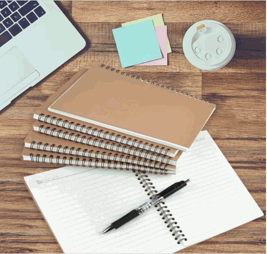 Personalized soft cover spiral notebooks on wooden desk with pen and sticky notes.