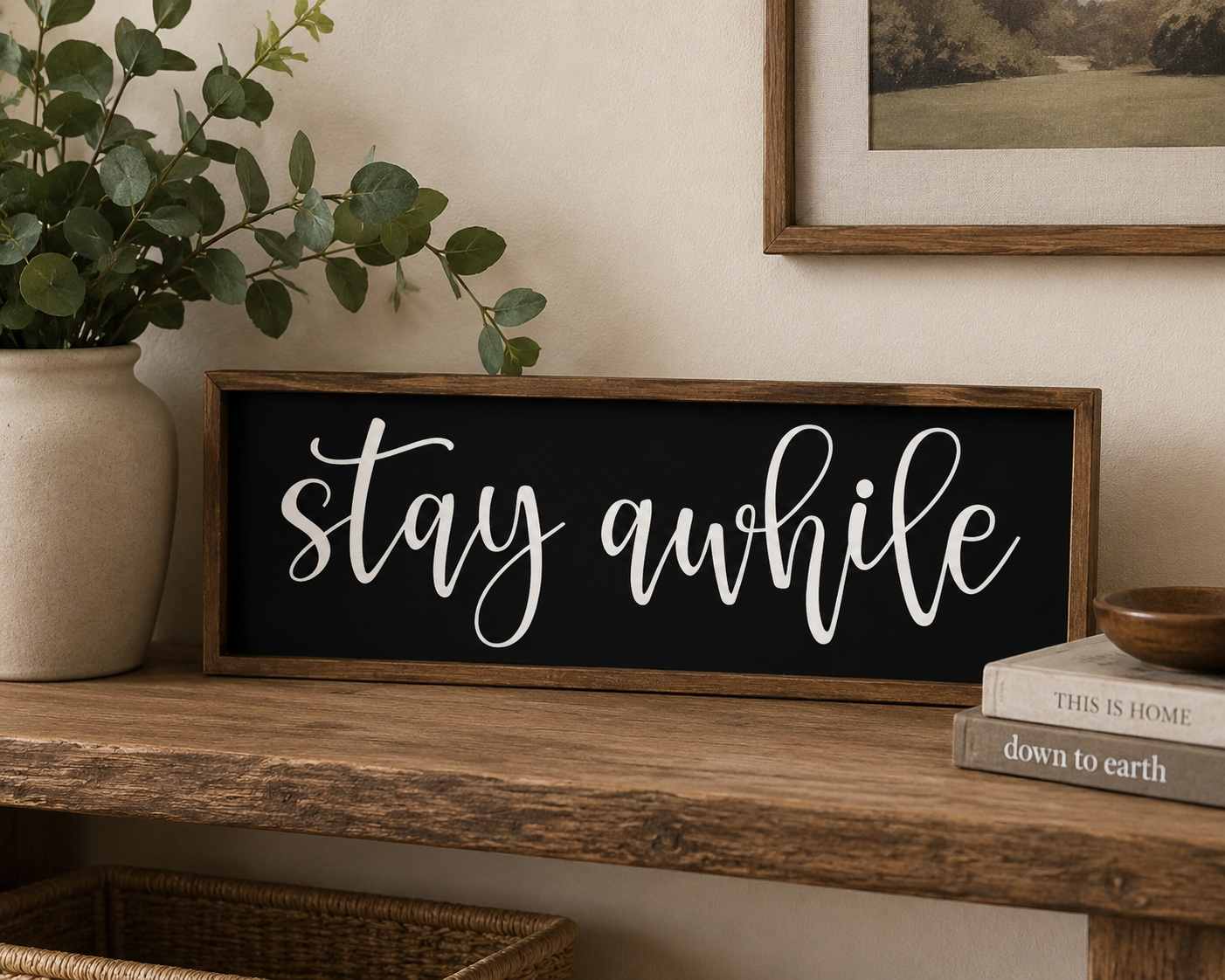 Decorative sign with 'stay awhile' on a wooden surface with a plant and books in the background.