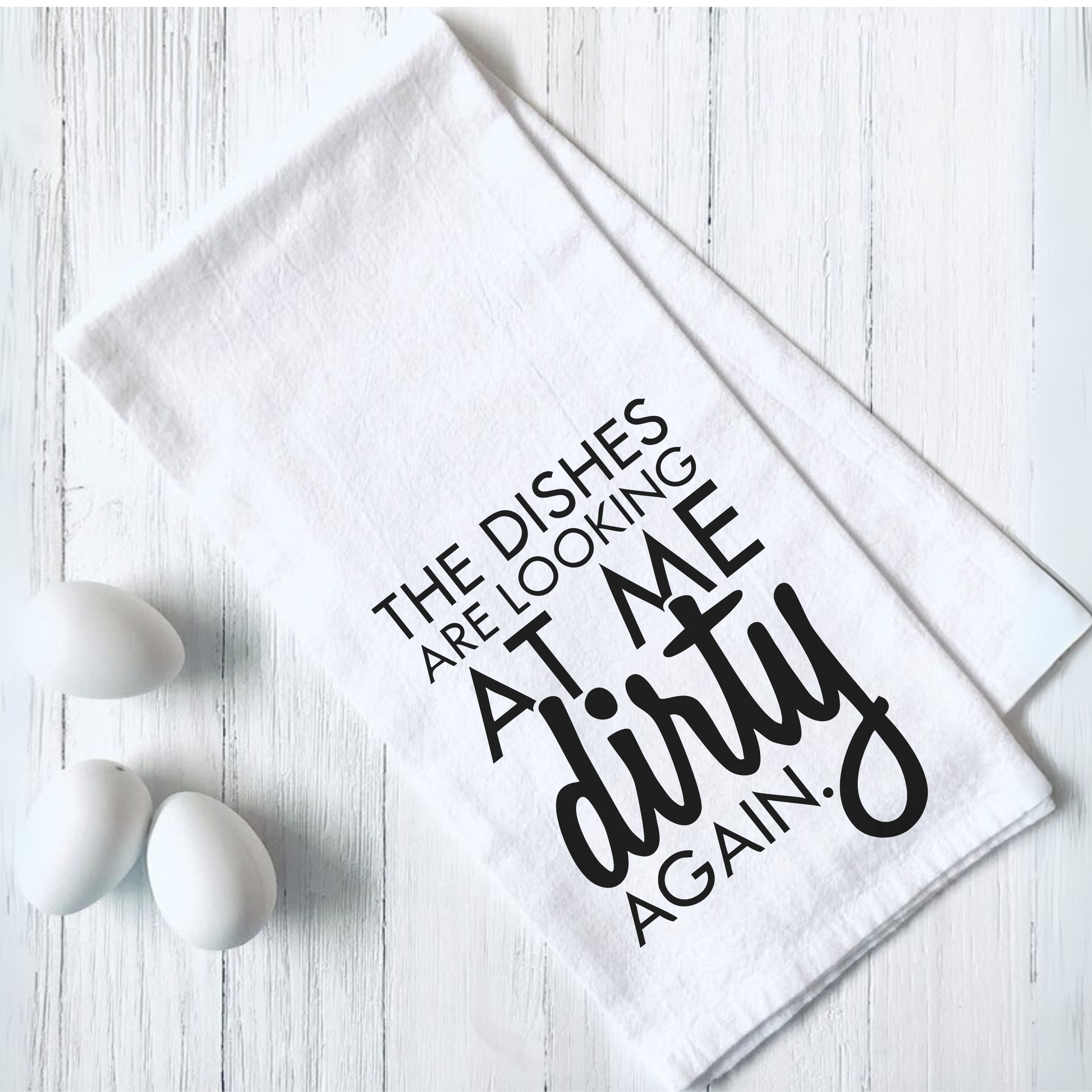 Funny tea towel with "The Dishes are Looking at Me Dirty Again" text design on white fabric