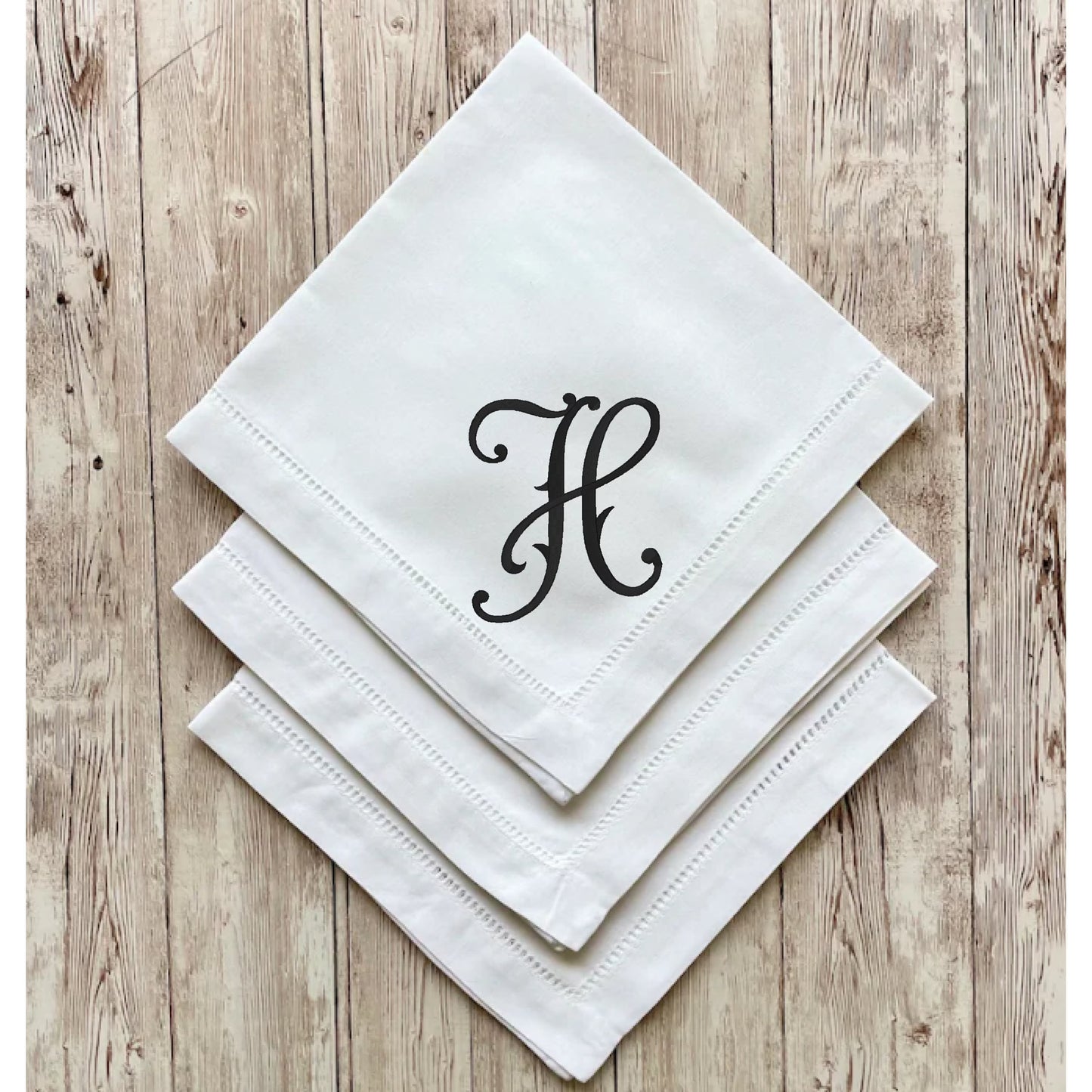 White napkins with a black monogram 'H' on a wooden surface