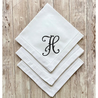 White napkins with a black monogram 'H' on a wooden surface