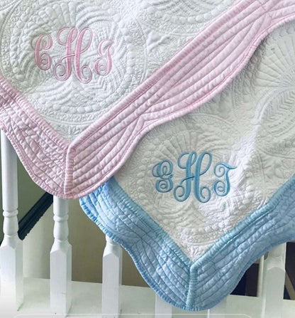 Personalized embroidered baby blanket with pink and blue trim, featuring custom monogram designs.