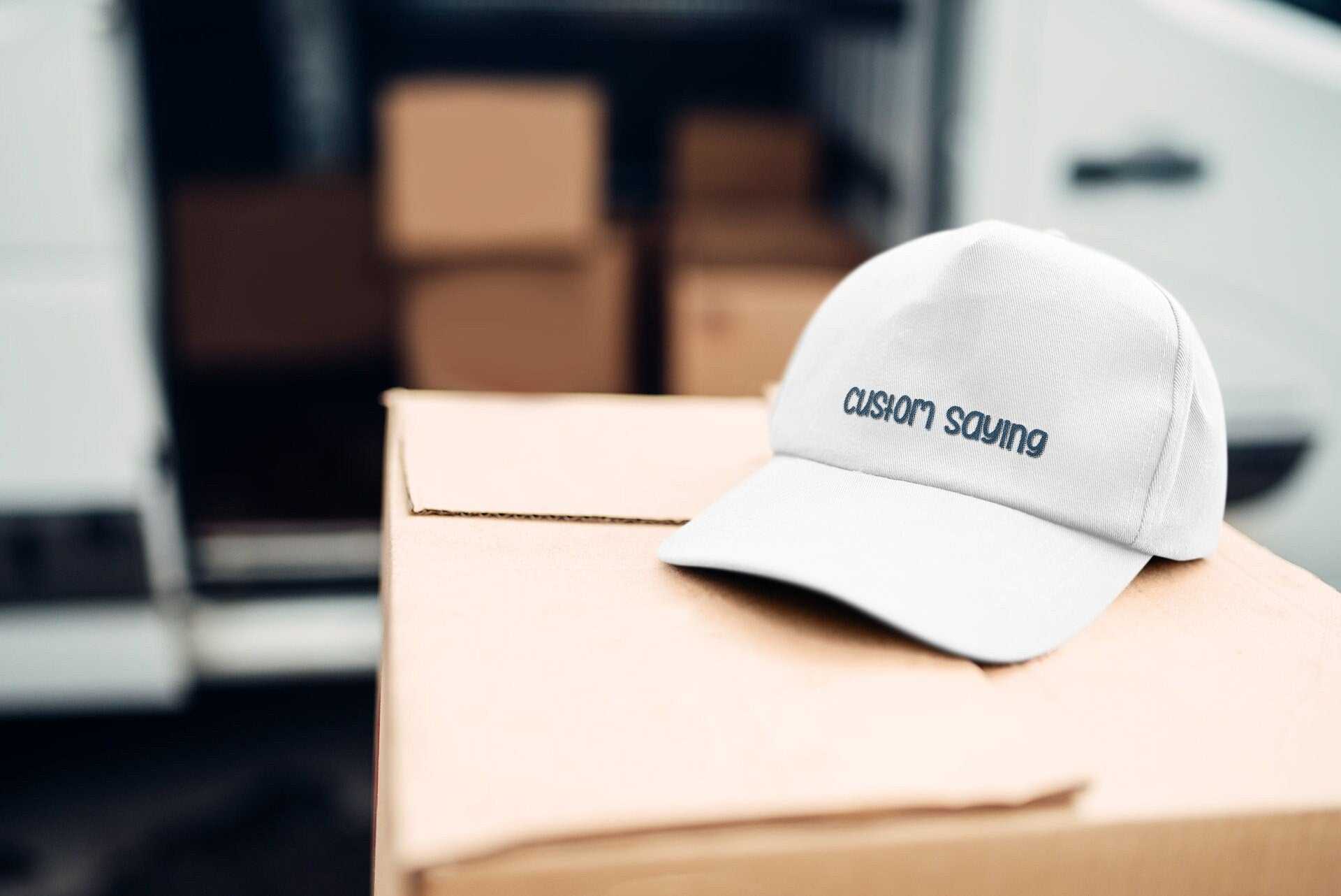 White personalized cap with custom embroidered text on front, unisex cotton dad hat on cardboard box