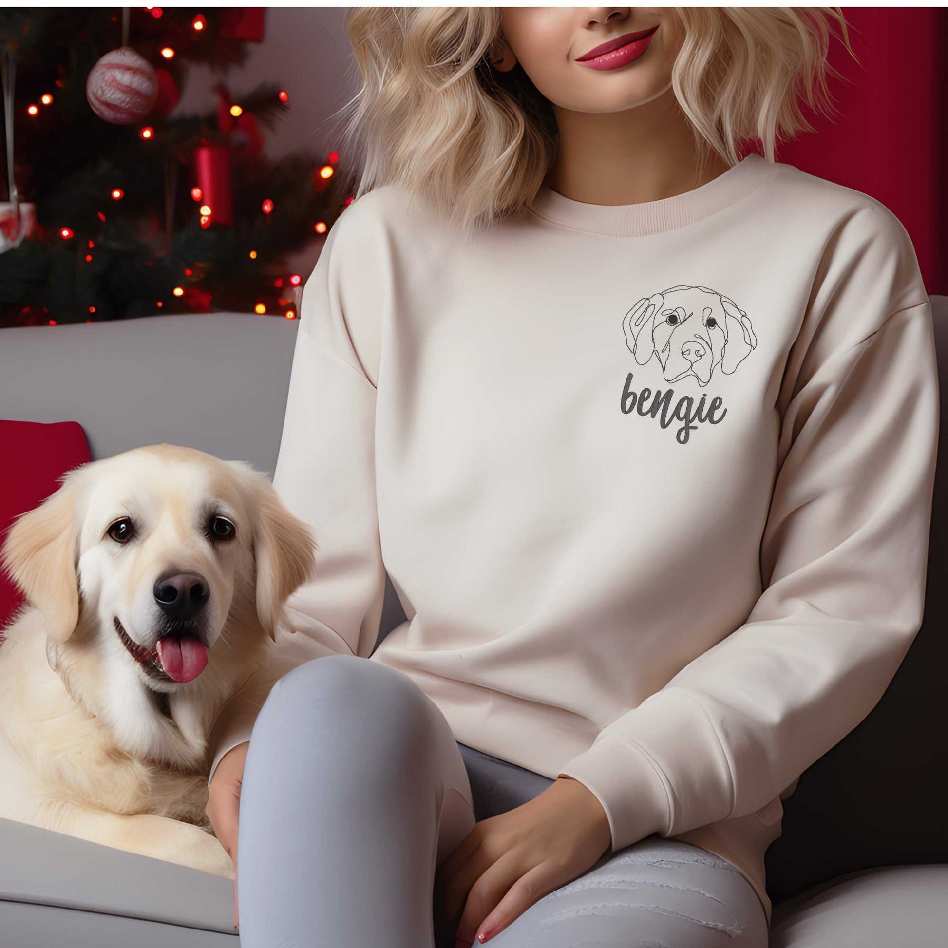 Woman wearing cream crewneck sweater with embroidered golden retriever head and name "bengie" in cursive font next to a golden retriever dog