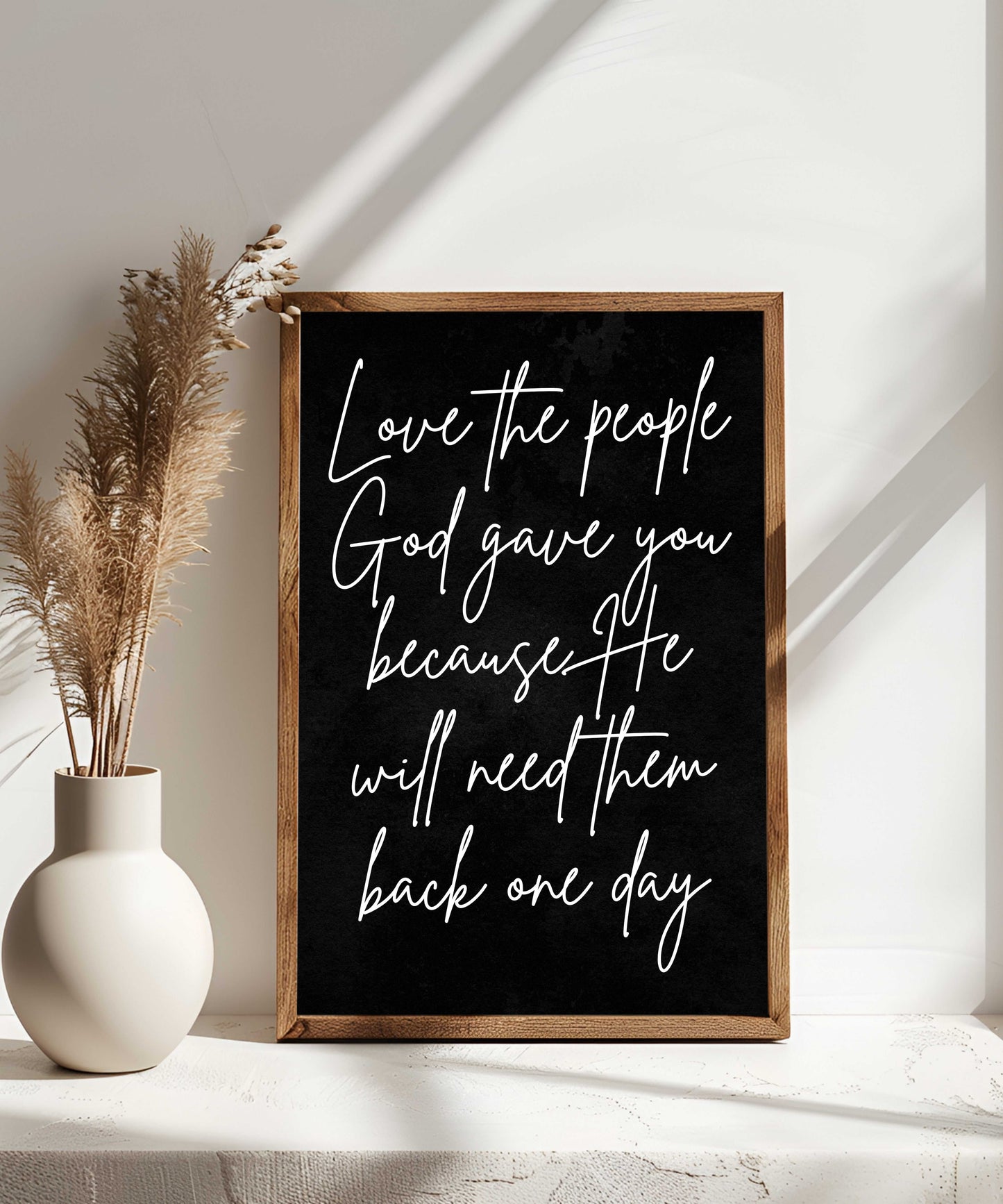 Farmhouse Christian wall art wood sign with "Love the people God gave you" script in a rustic frame next to a vase with dried pampas grass.