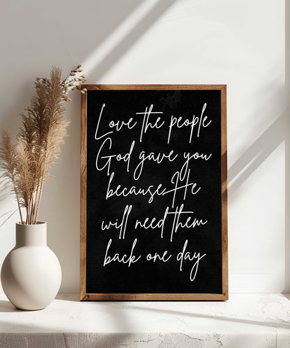 Farmhouse Christian wall art wood sign with "Love the people God gave you" script in a rustic frame next to a vase with dried pampas grass.