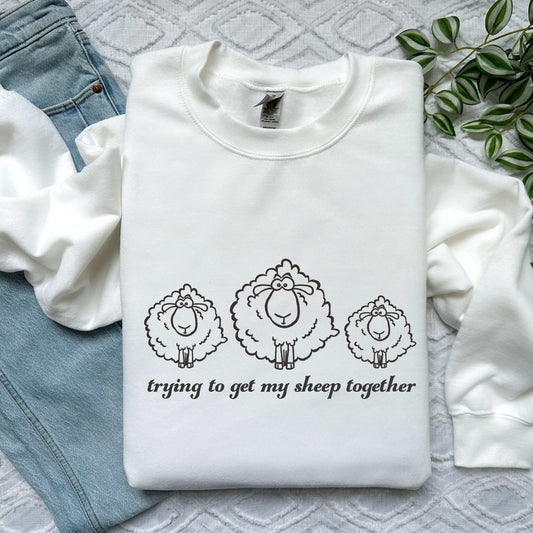 Cozy embroidered sweatshirt featuring three fluffy sheep and the phrase "Trying to Get My Sheep Together," perfect for