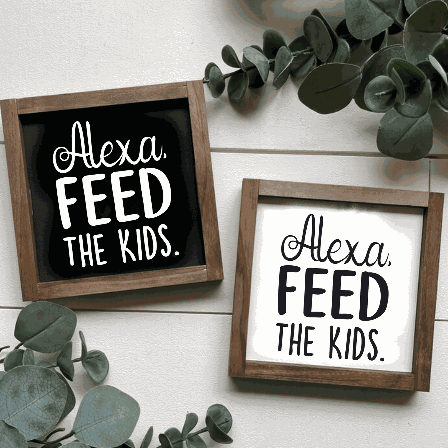 Handcrafted "Alexa, Feed The Kids" framed wood sign with black and white lettering, surrounded by greenery.