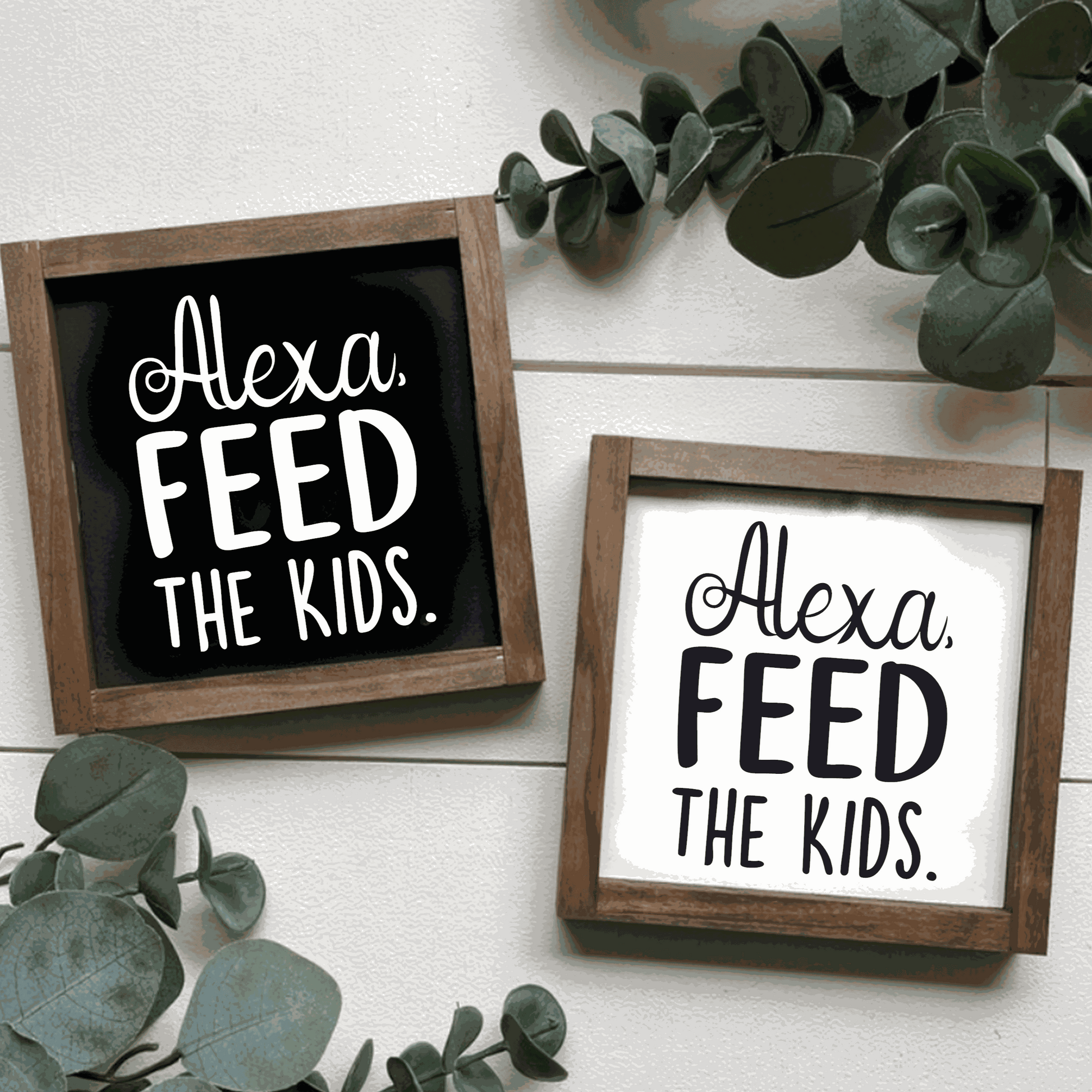 Handcrafted "Alexa, Feed The Kids" framed wood sign with black and white lettering, surrounded by greenery.