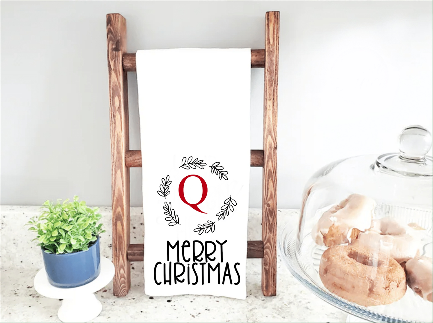 Personalized monogram Christmas tea towel with initial and wreath design displayed on a wooden rack.