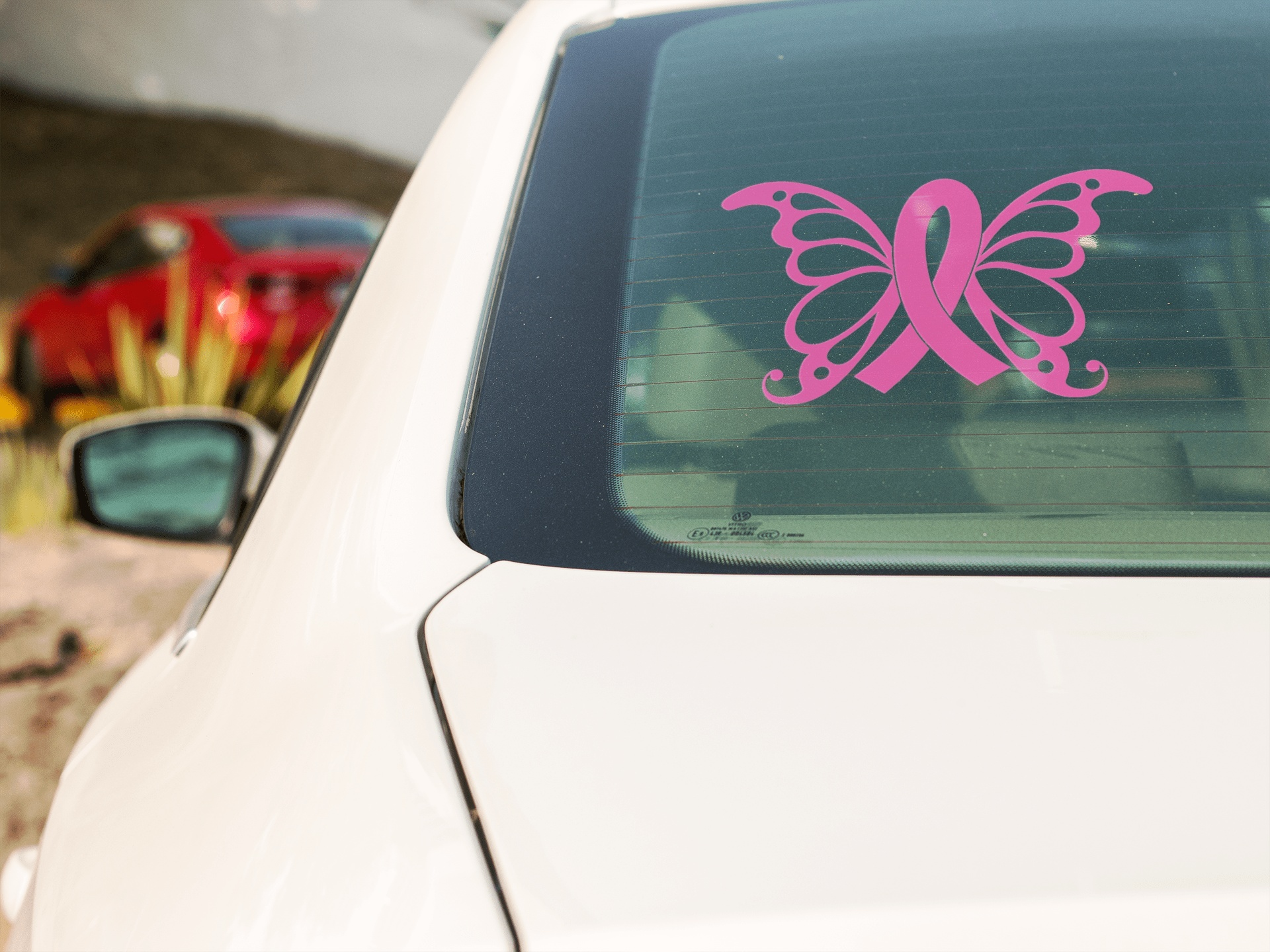Pink butterfly cancer awareness car sticker on rear window of white vehicle.