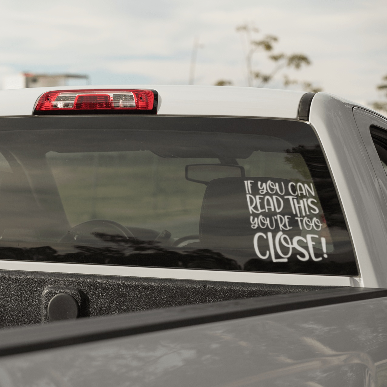 "If You Can Read This You're Too Close" car decal on truck window, durable vinyl sticker for outdoor use.