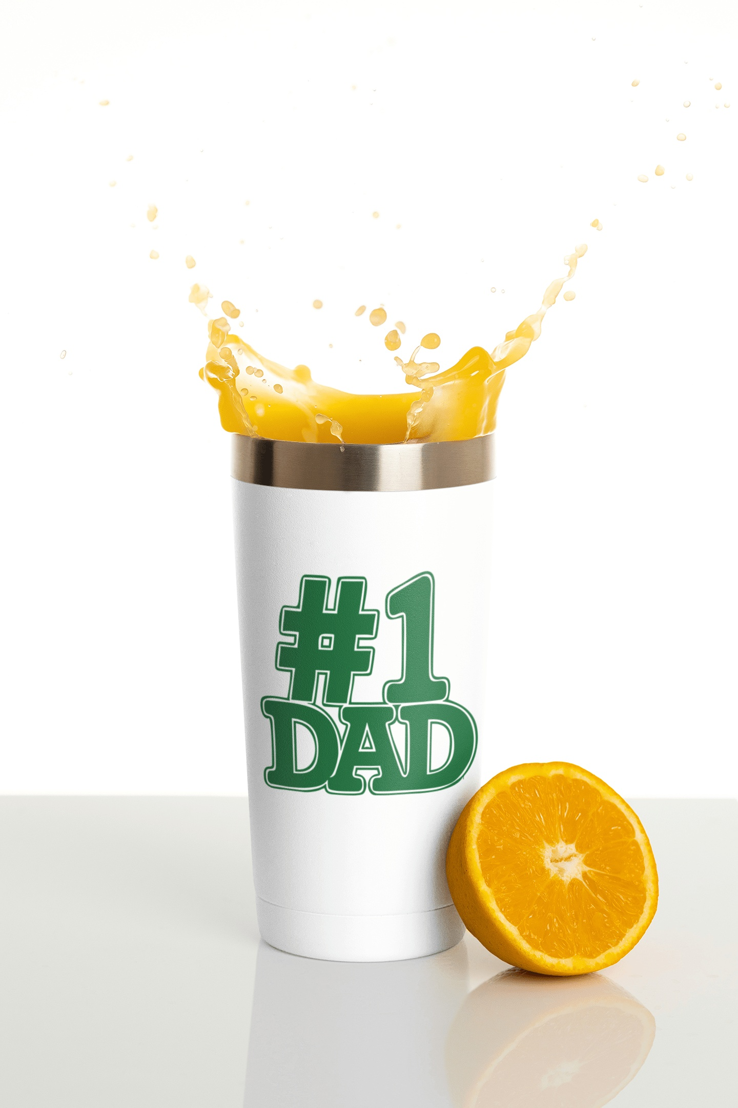 White tumbler with a green #1 Dad sticker and orange juice splash next to a halved orange