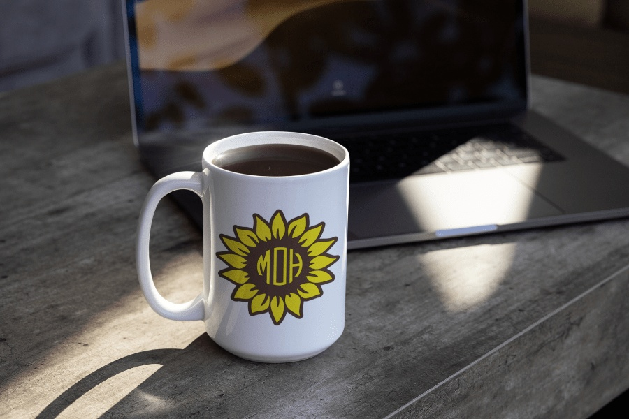 Personalized sunflower vinyl monogram decal on a white mug near a laptop.