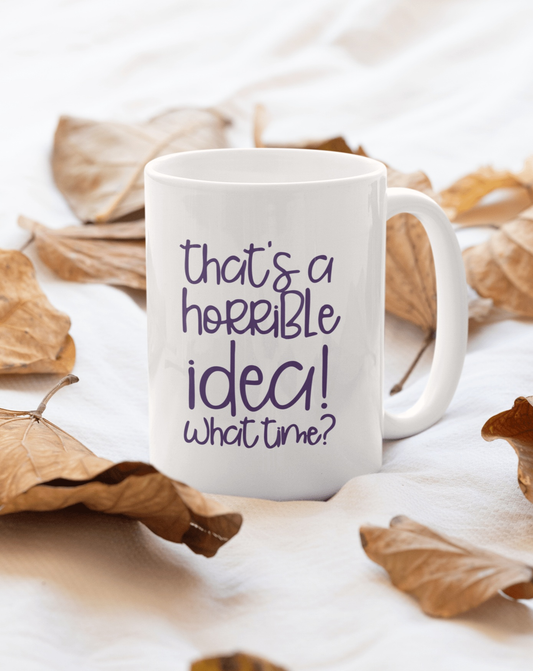 Funny ceramic mug with "That's a Horrible Idea, What Time?" saying, surrounded by autumn leaves.