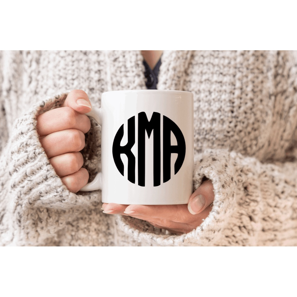 Person holding a white mug with a black vinyl monogram decal "KMA".