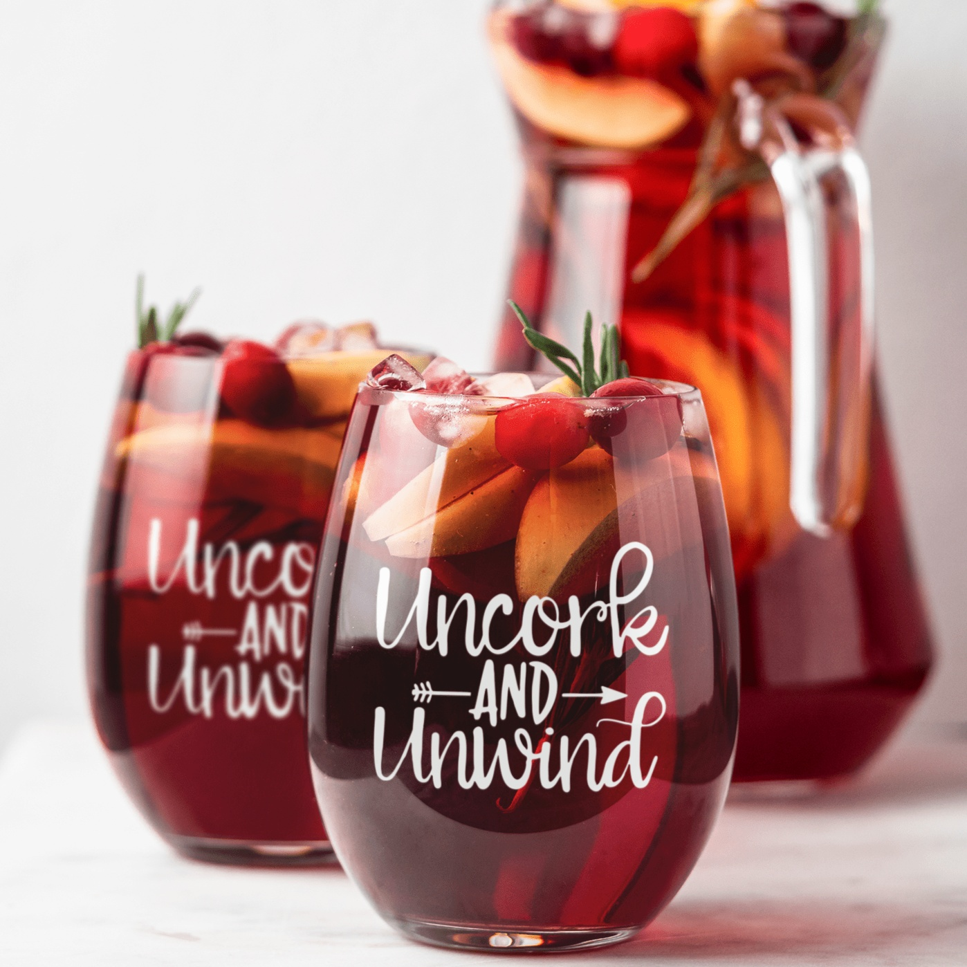 Stemless wine glass with "Uncork and Unwind" engraved, filled with sangria, ideal for gifting.