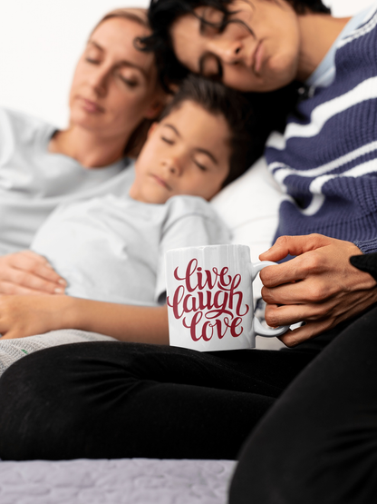 Ceramic coffee mug with "Live, Laugh, Love" design, held by person sitting with family.