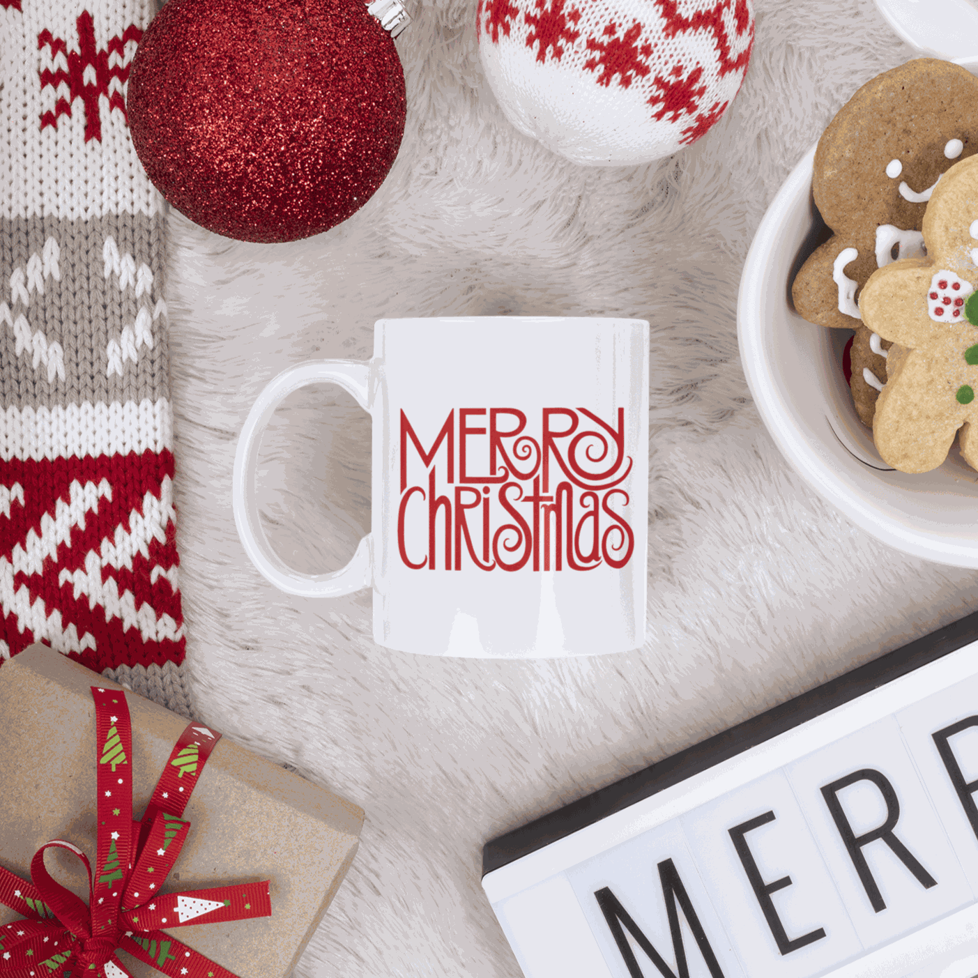 Merry Christmas mug with red festive design on white background, surrounded by holiday decorations and cookies.