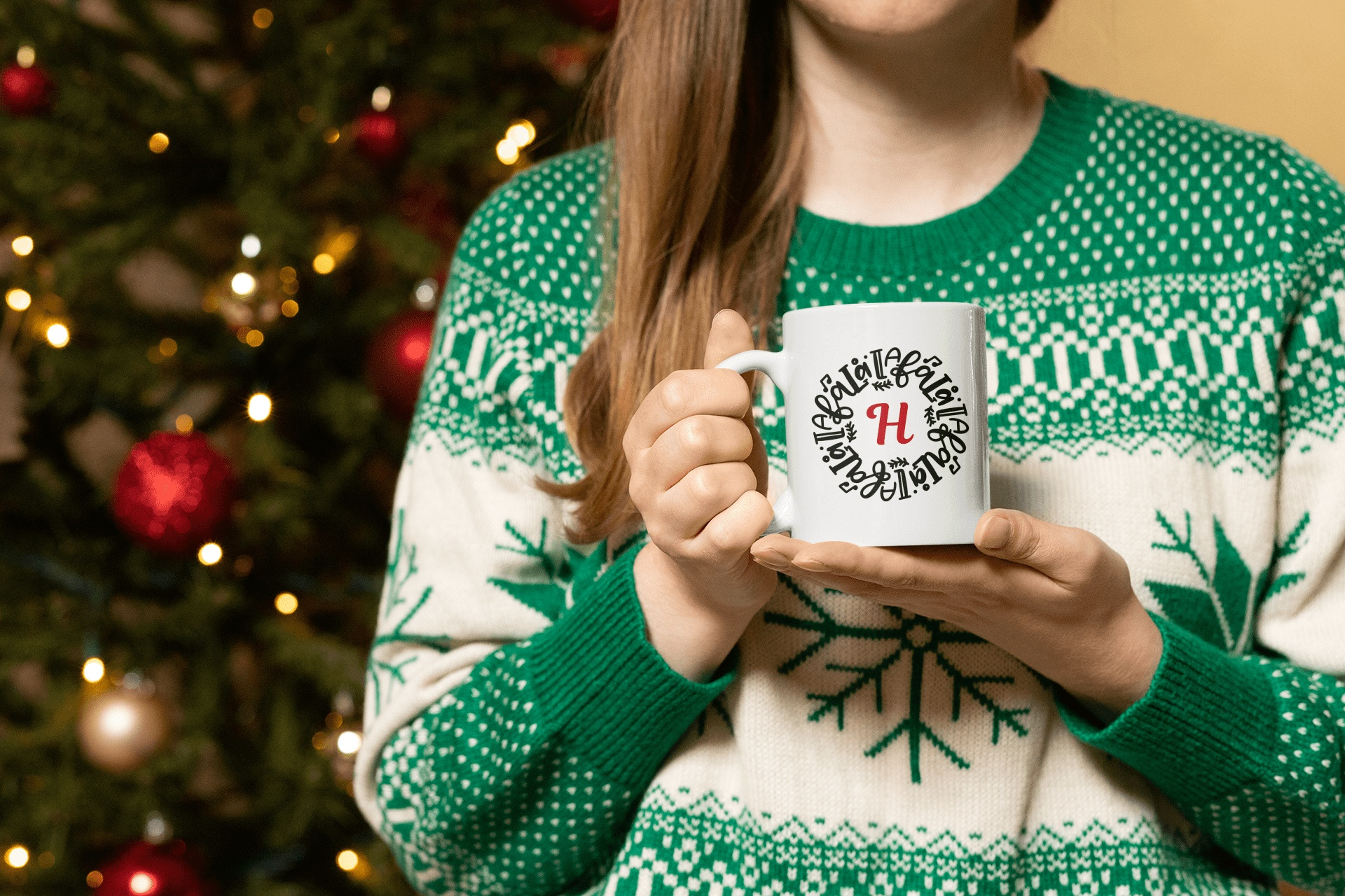 Woman holding personalized Christmas mug near tree, initial H design, festive sweater.