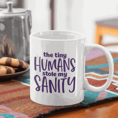 Ceramic mug with the quote "The Tiny Humans Stole my Sanity" in purple lettering, ideal for new parents.