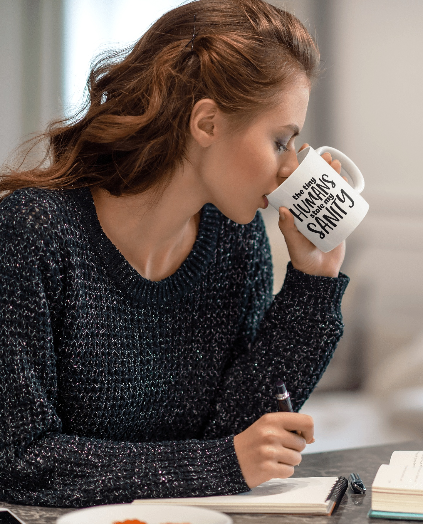 Woman sipping from ceramic mug with "The Tiny Humans Stole my Sanity" inscription.